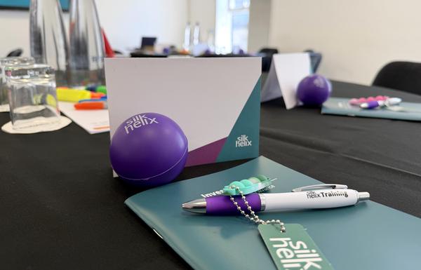 Photograph of a Silk Helix training room setup, including workbook, stress ball, pen and name card.